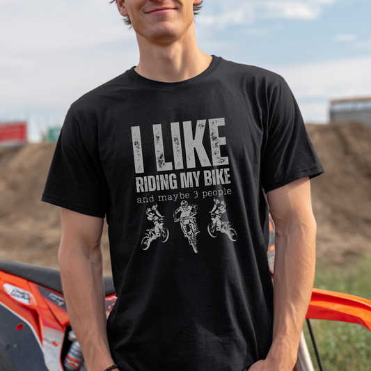 Person wearing a black t-shirt with 'I LIKE RIDING MY BIKE and maybe 3 people' text and graphics, standing in front of a motorcycle.