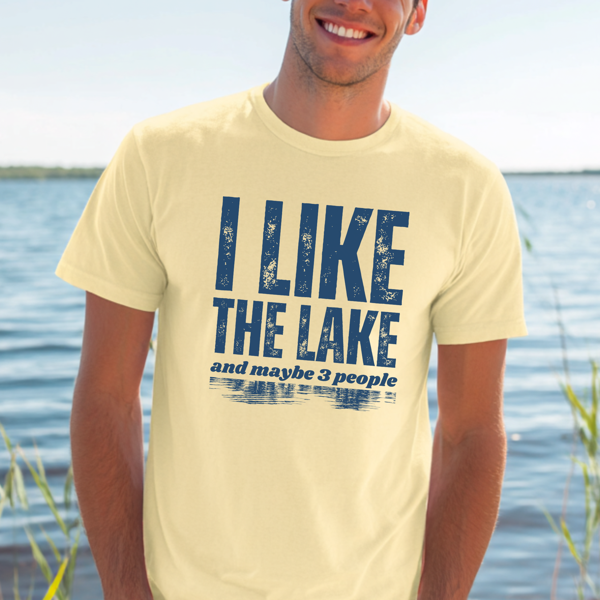 Man wearing a yellow t-shirt with 'I LIKE THE LAKE and maybe 3 people' text by a lake.