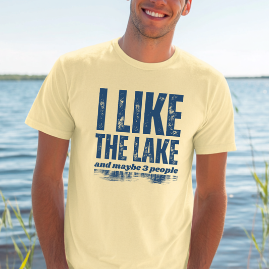 Man wearing a yellow t-shirt with 'I LIKE THE LAKE and maybe 3 people' text by a lake.