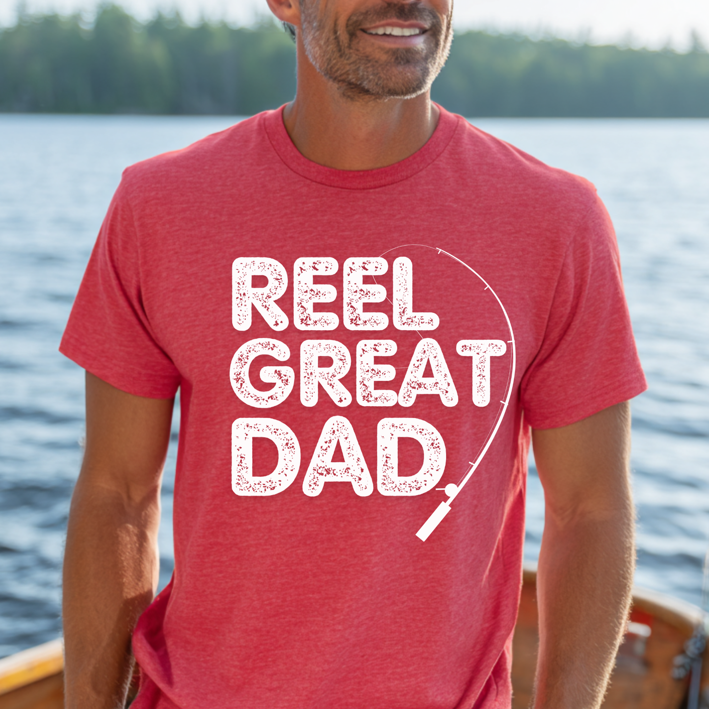 Man wearing a red 'REEL GREAT DAD' t-shirt by a body of water.