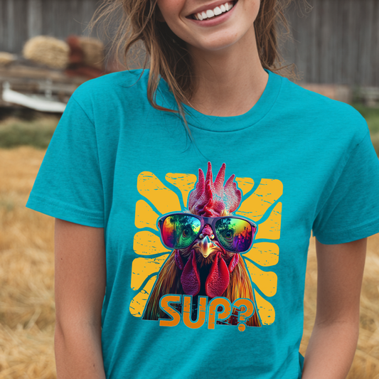 Person wearing a turquoise t-shirt with a rooster graphic and 'SUP?' text in a barn setting.