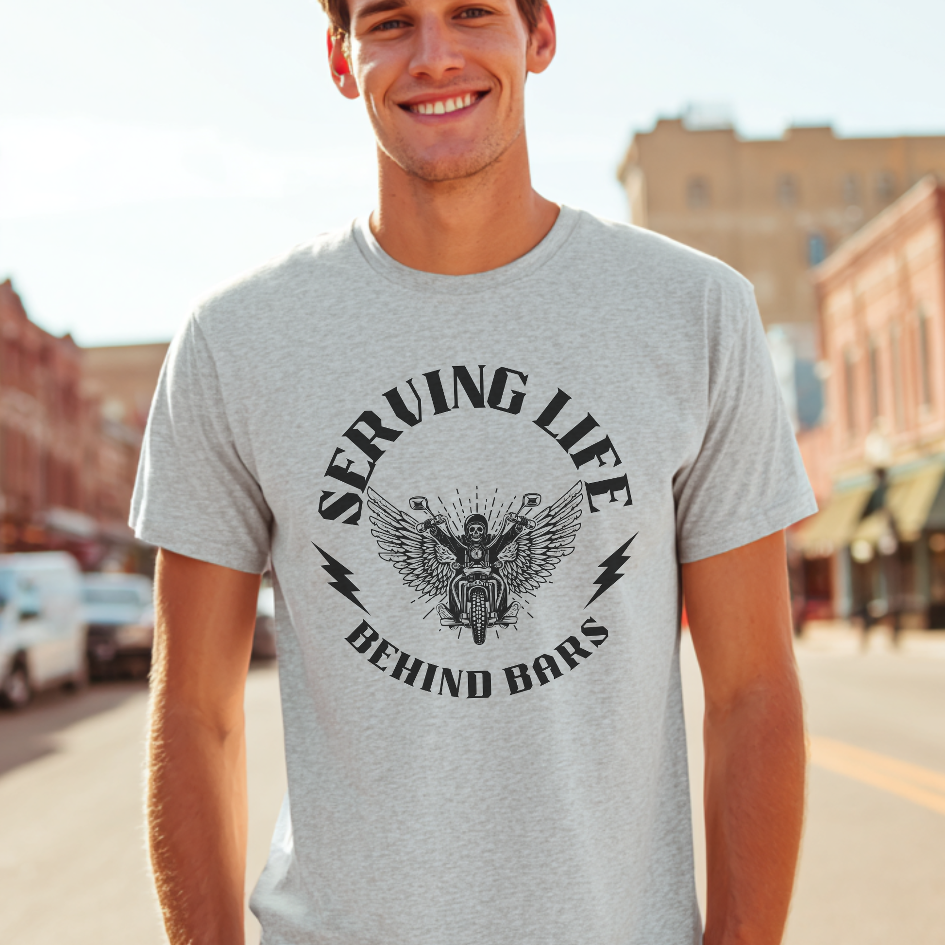 Man wearing a gray t-shirt with a graphic design and text, standing on a street.