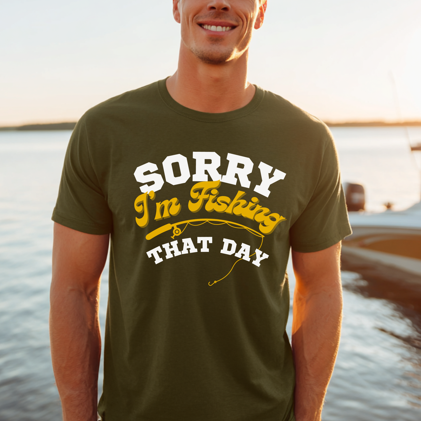 Man wearing a green t-shirt with 'Sorry I'm Fishing That Day' text by a lake.