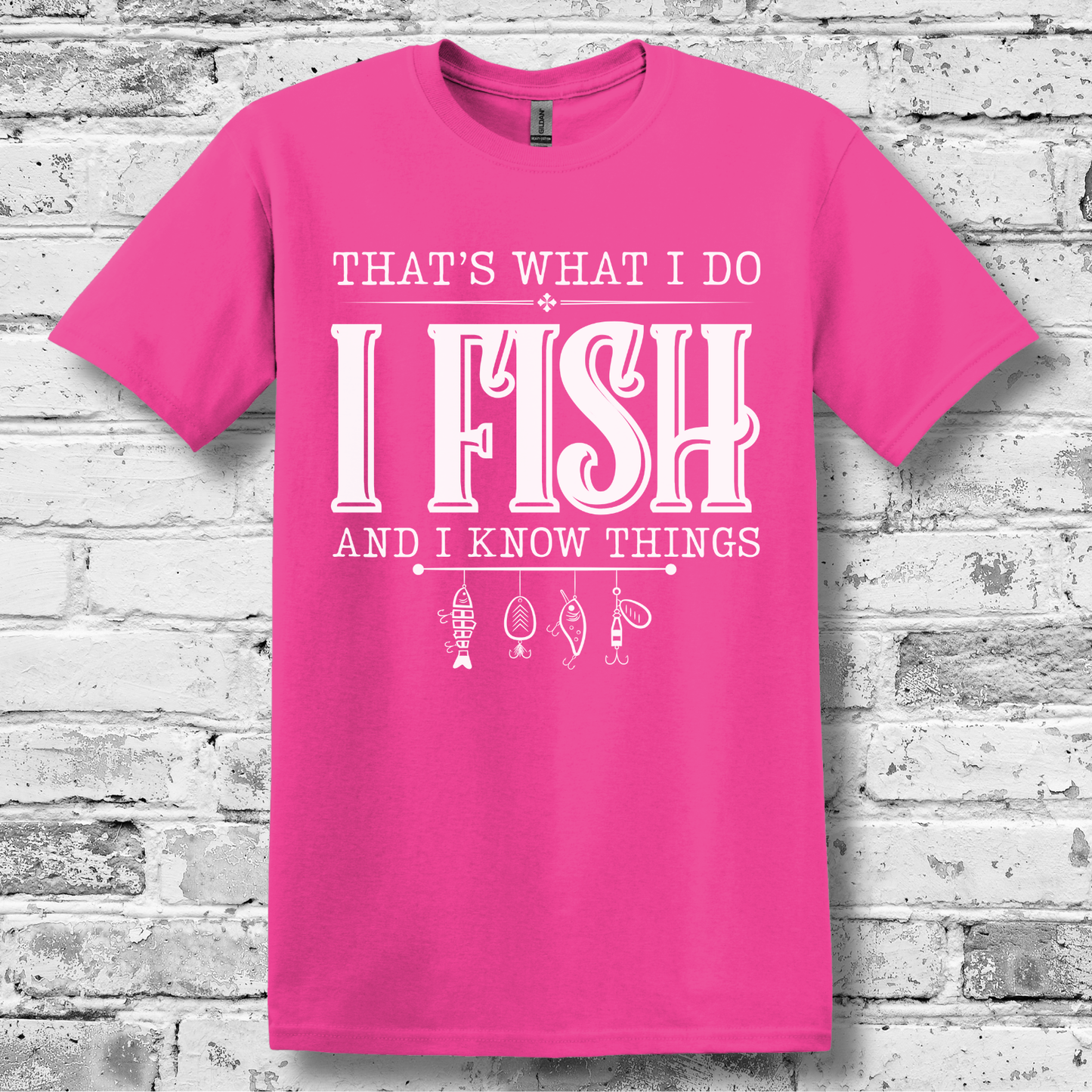 Pink t-shirt with white text and fishing-related graphics on a brick wall background
