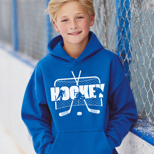 Child wearing a blue hoodie with a hockey design, standing in front of a hockey rink.