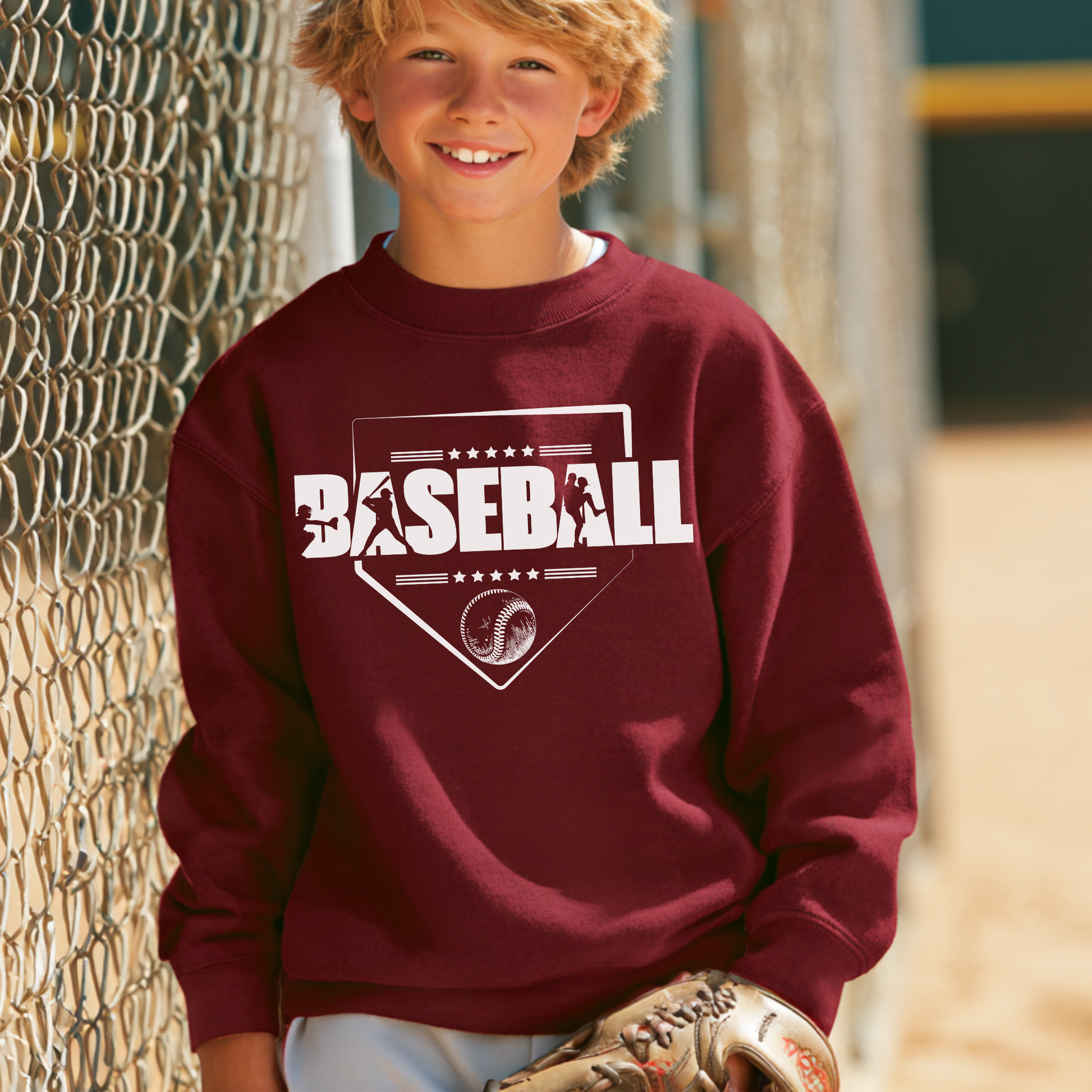 Child wearing a maroon sweatshirt with 'BASEBALL' printed on it, standing next to a chain-link fence.