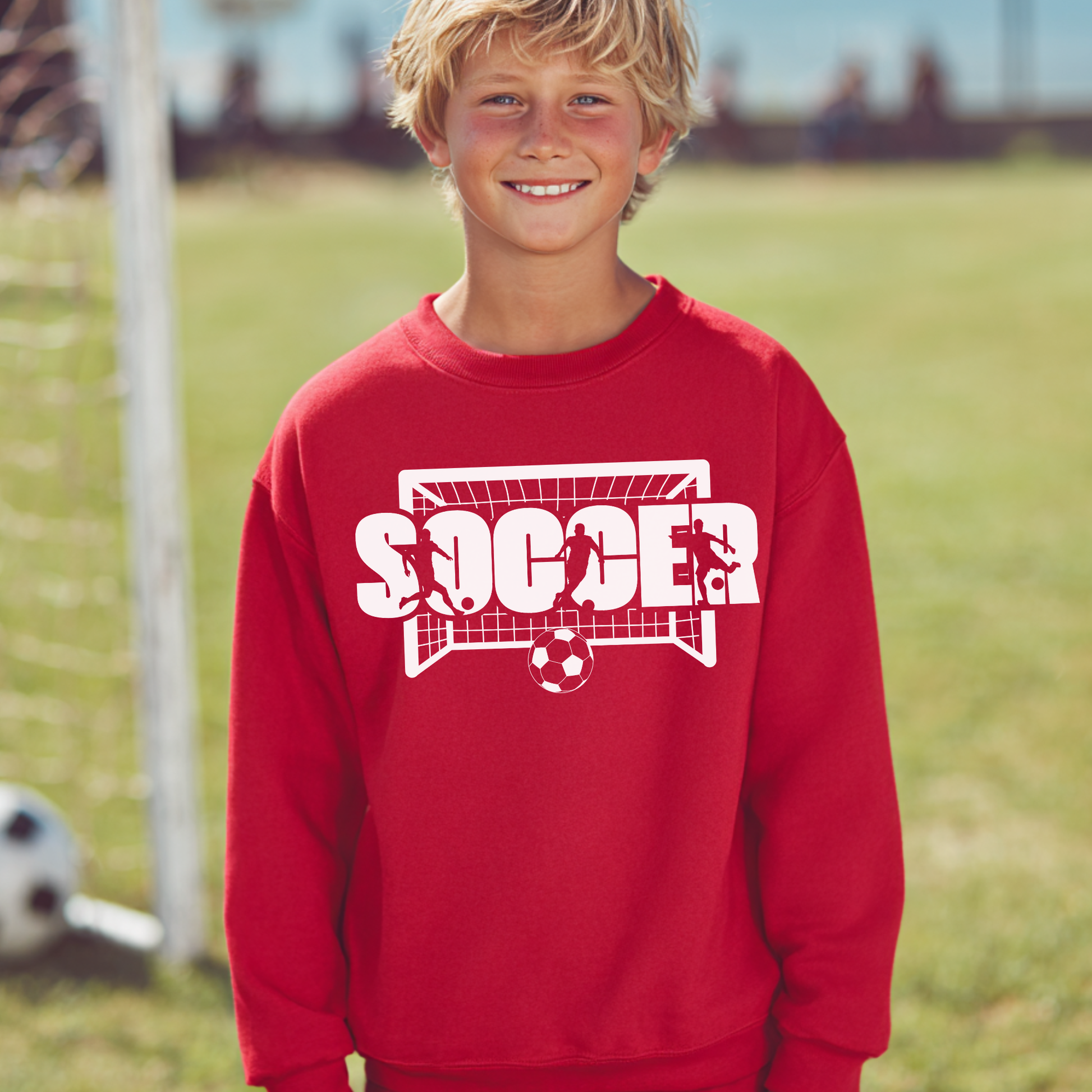 Child wearing a red sweatshirt with 'SOCCER' printed on it, standing on a grassy field.
